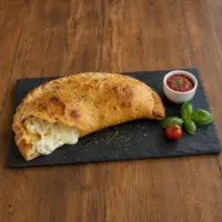 Three cheese calzones filled with ricotta, mozzarella and Parmesan beside warm tomato sauce