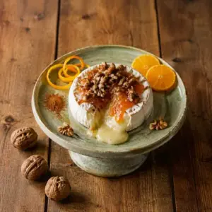 Warm baked Brie topped with orange marmalade and spiced walnuts on a rustic wooden table.