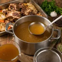 Classic Meat Stock simmering with roasted bones, vegetables, and fresh herbs in a large stockpot.