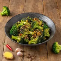 Air-fried Sichuan broccoli with chili oil, garlic and ginger in a black bowl on a rustic wooden table.