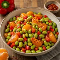 Sweet Spicy Edamame with mandarin oranges, red bell pepper, and soy glaze served in a rustic bowl.