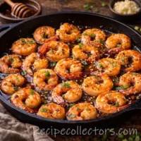 honey garlic shrimp coated in a sticky glaze served in a skillet on a very dark heavy rustic oak wooden table