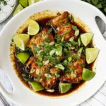 Sticky honey lime chicken skillet on a dark heavy rustic oak wooden table with visible grain and fresh limes
