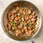 spicy cashew chicken in a skillet on a very dark heavy rustic oak wooden table
