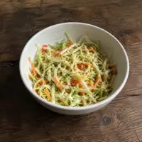 Fresh cabbage and carrot slaw with coriander and red chilli in a simple ceramic bowl on a rustic wooden table.